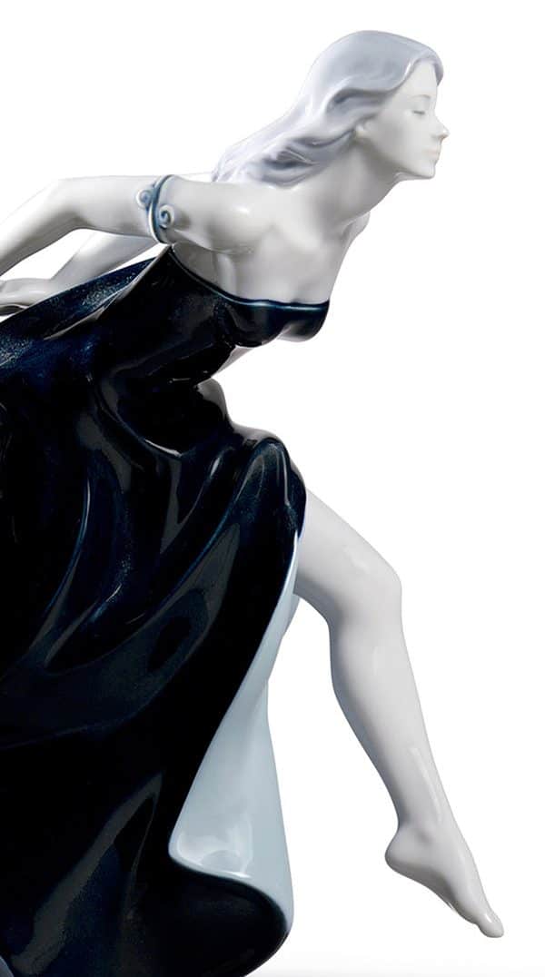 Glossy porcelain figurine of two beautiful women with long and voluptuous dresses of a deep blue degraded color. Close up of leading lady leaping forward.