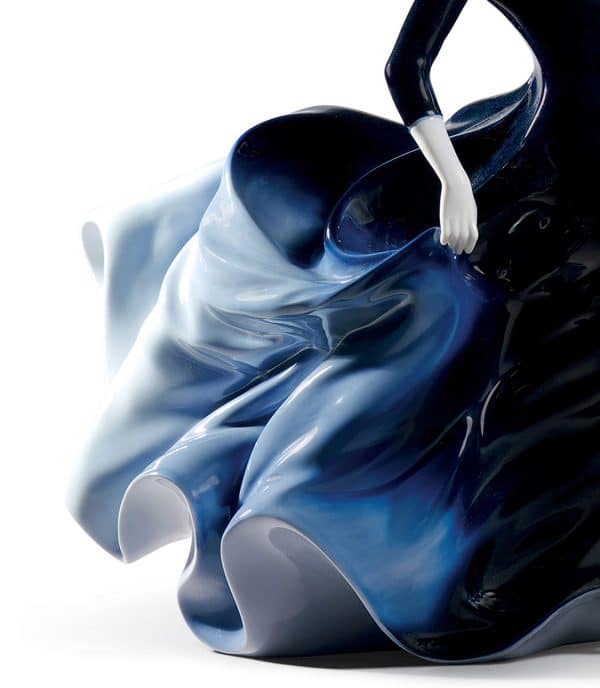 Glossy porcelain figurine of two beautiful women with long and voluptuous dresses of a deep blue degraded color. close up of the flowing ballroom dress.