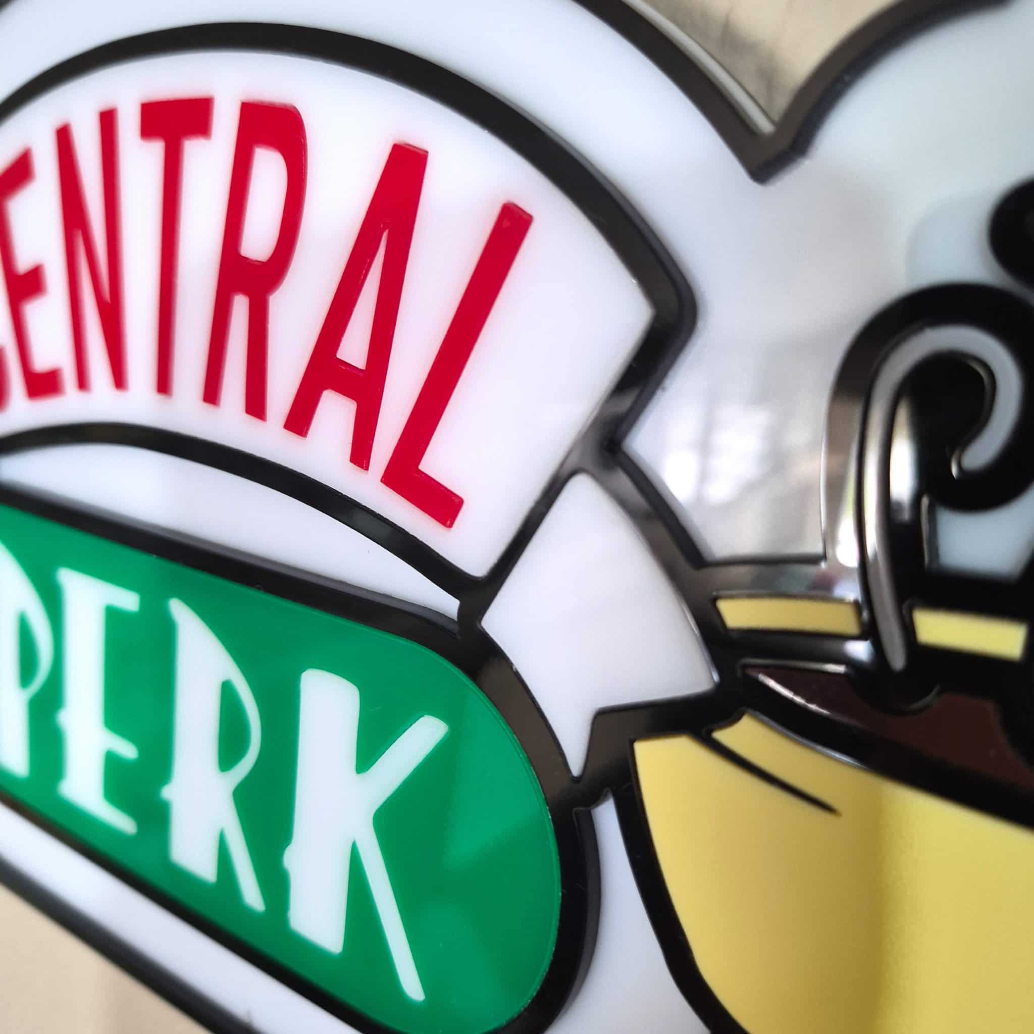 Close-up macro detail of a 3D acrylic Central Perk sign showing the raised white steam, yellow coffee cups, and seamless red and white flush-inlaid text.