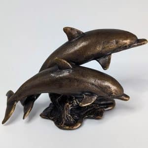 Solid bronze sculpture of two dolphins leaping over a textured ocean wave with warm patina finish by Marquise Jewellery