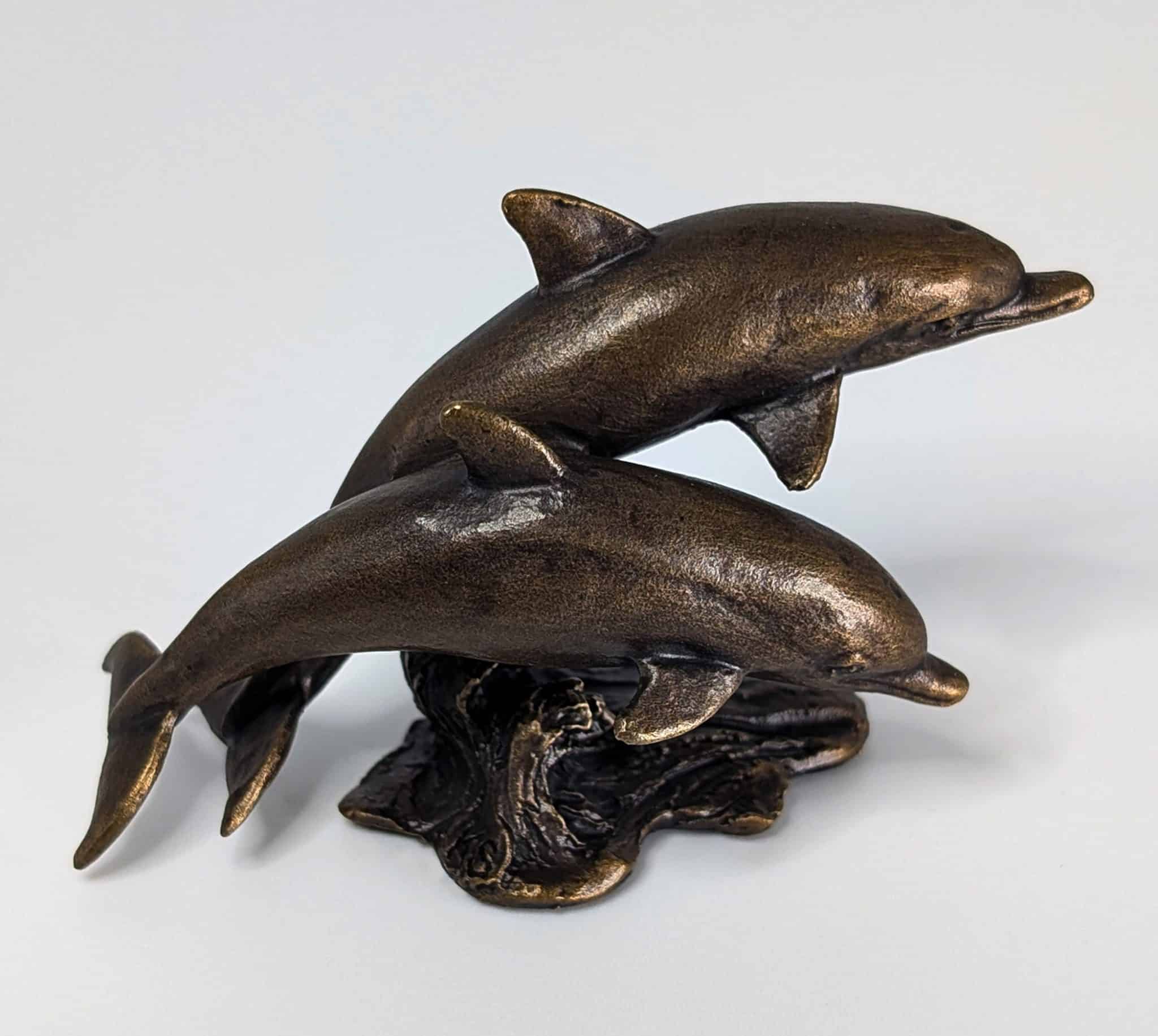 Solid bronze sculpture of two dolphins leaping over a textured ocean wave with warm patina finish by Marquise Jewellery